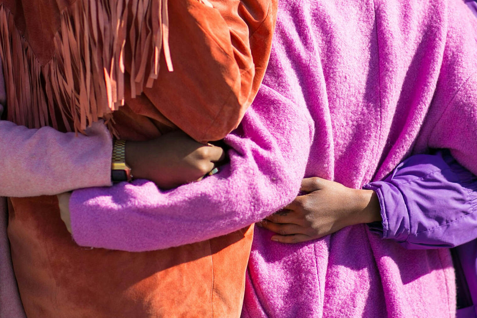 Four women holding each other's sides wearing bright pinks and oranges.